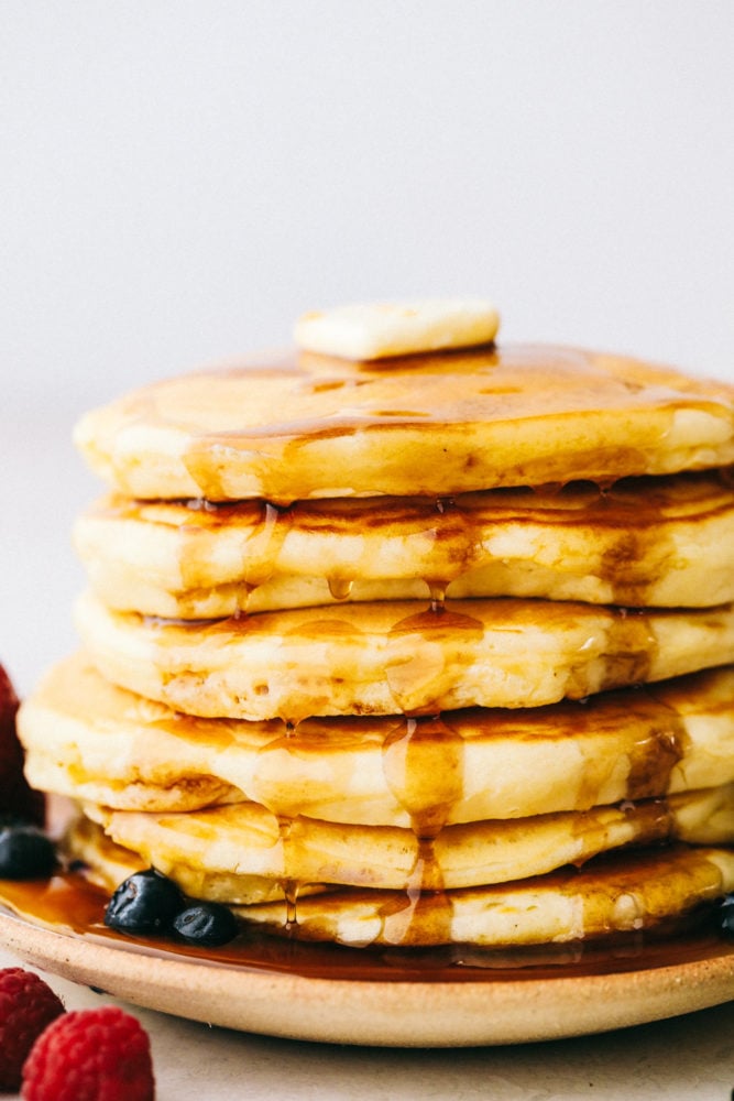 Grandma's homemade fluffy pancakes are the ultimate comfort breakfast! They're light and airy, yet satisfyingly filling, making them the perfect morning treat. Fluffy pancakes stacked on top of each other with a slice of butter, syrup and fresh fruit.