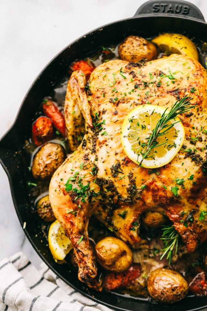 Garlic roasted chicken with vegetables is a whole chicken rubbed with an herb butter then stuffed with a mixture of seasonings. Roasted in a large skillet combined with fresh, flavorful vegetables!ย Garlic roasted chicken with vegetables on a skillet after being cooked and garnished with lemon on top.