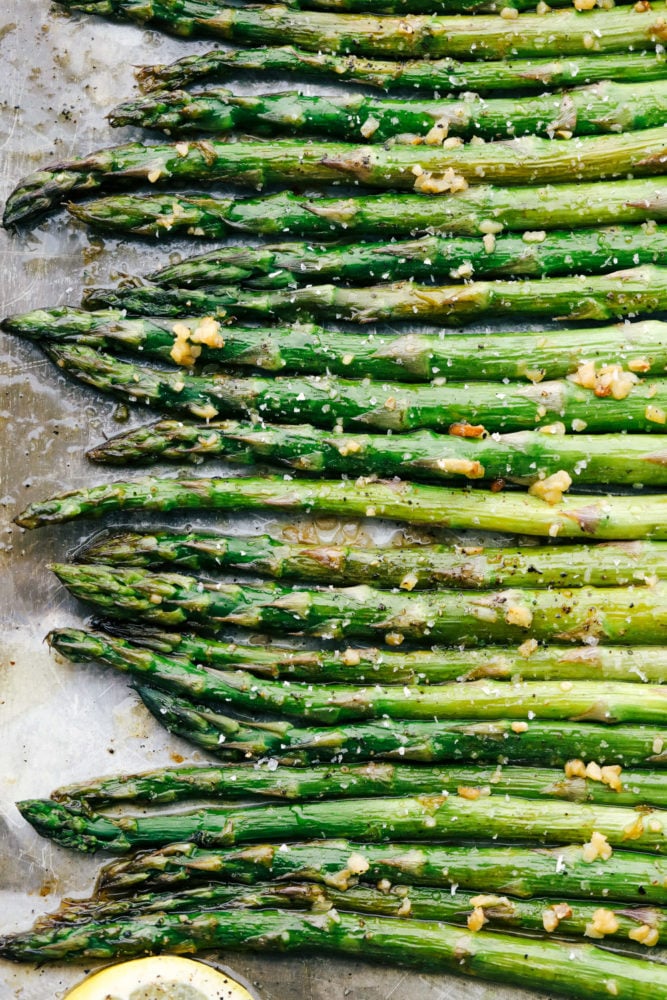 This lemon honey garlic asparagus recipe has a crisp outside with a tender inside cooked in a lemon, honey marinade with minced garlic. This asparagus compliments any main dish and adds a colorful feel to the table! Asparagus laying flat on a baking sheet showing just he heads of the asparagus.