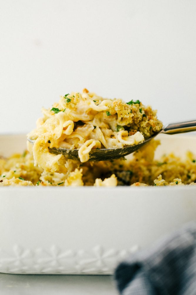 This tuna noodle casserole is a family favorite that is filled with thick noodles, vegetables and tender chunks of tuna fish. All baked together in one pan in 30 minutes! Tuna noodle casserole lifted up from the pan with a metal spoon.