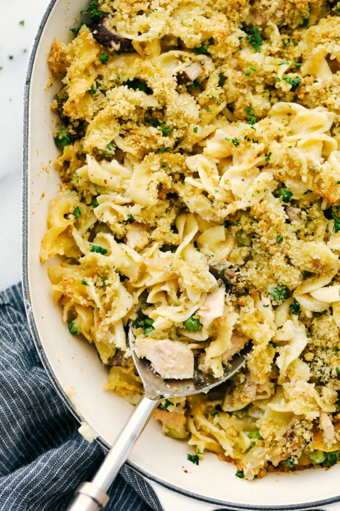This tuna noodle casserole is a family favorite that is filled with thick noodles, vegetables and tender chunks of tuna fish. All baked together in one pan in 30 minutes! Tuna casserole in a casserole dish with a spoon in them.