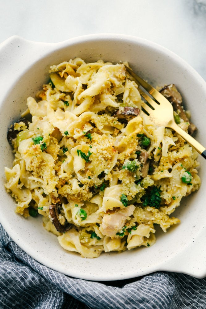 This tuna noodle casserole is a family favorite that is filled with thick noodles, vegetables and tender chunks of tuna fish. All baked together in one pan in 30 minutes! Tuna noodle casserole in a bowl with a fork r