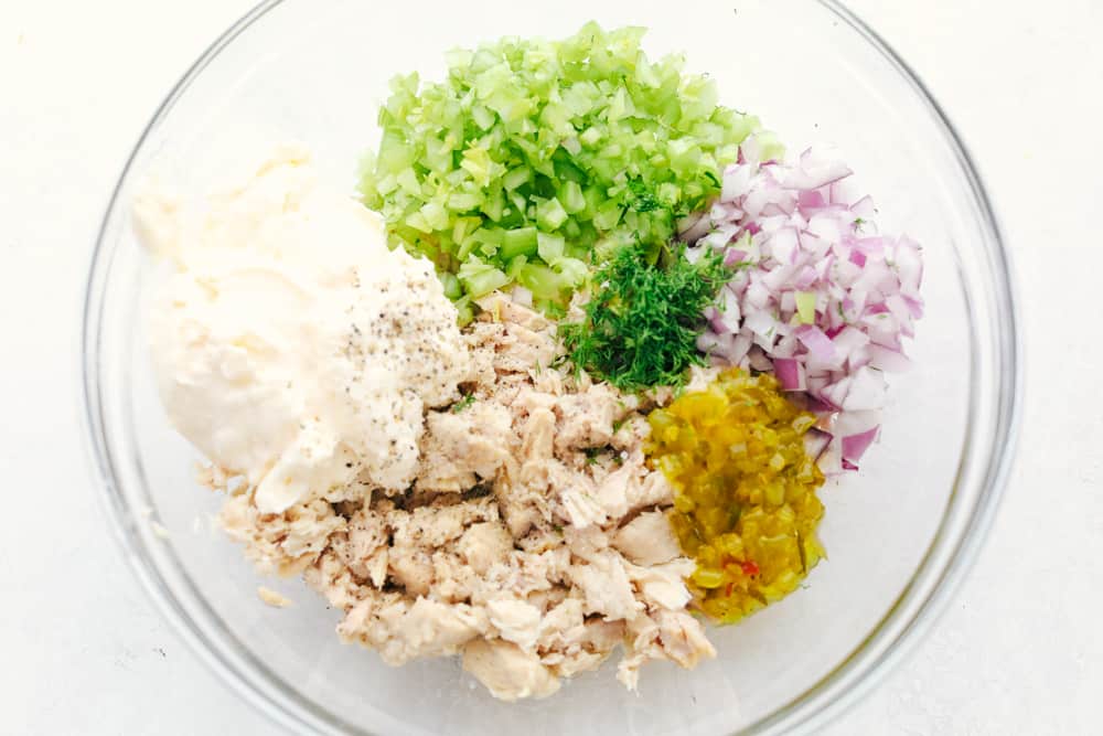 This tuna salad is a classic favorite that mixes up well and tastes rich and creamy with slices of crisp celery and red onions for that added crunch. All comes together quickly and easily with pantry ingredients! Tuna salad ingredients all separated in sections in the bowl.