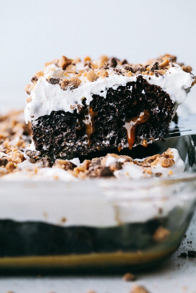 This better than anything cake is a chocolate cake filled with caramel pockets, layered with cool whip and topped with heath bites making ย this cake extremely moist and flavorful in every bite! Make this your next party cake!ย Better than anything cake being sliced and held in the air for the photo using a spatula.