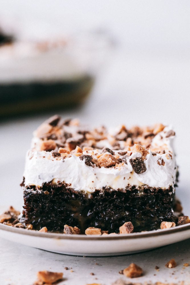 This better than anything cake is a chocolate cake filled with caramel pockets, layered with cool whip and topped with heath bites making ย this cake extremely moist and flavorful in every bite! Make this your next party cake!ย Better than anything cake sliced in a square on a white plate.
