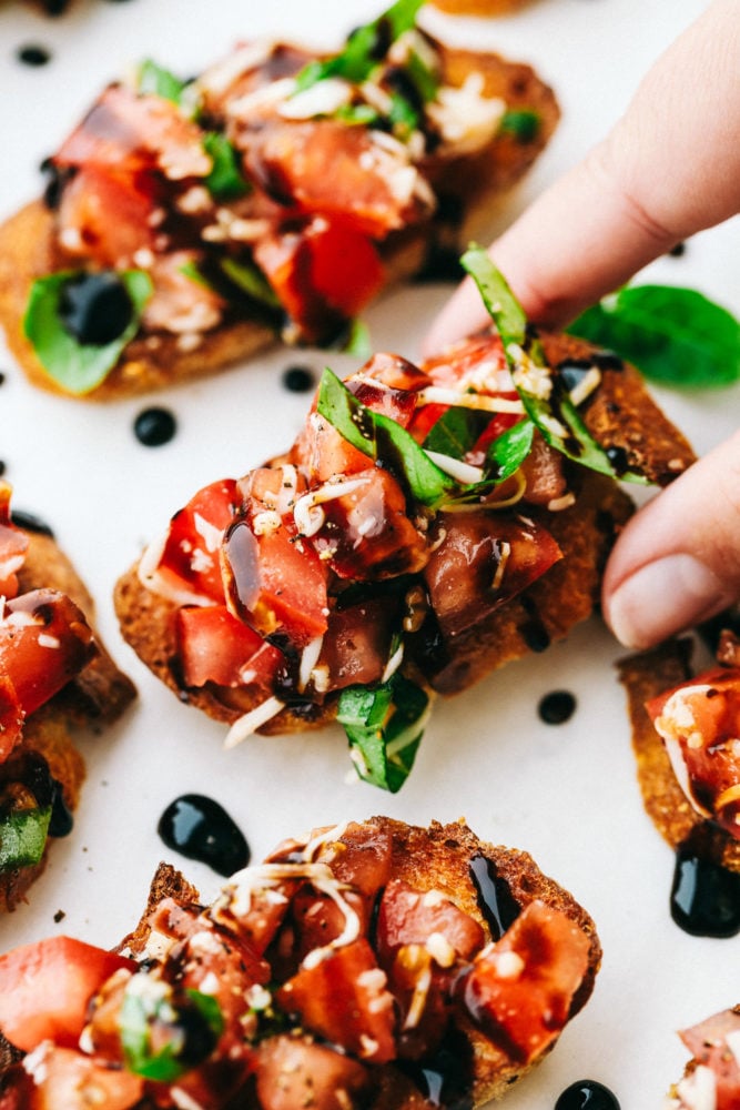 This bruschetta is easy to make with fresh, ripe Roma tomatoes, shredded mozzarella cheese and drizzled with balsamic vinaigrette over top of a French baguette. Bruschetta comes together quickly and easily!ย Bruschetta presented on a white plate.