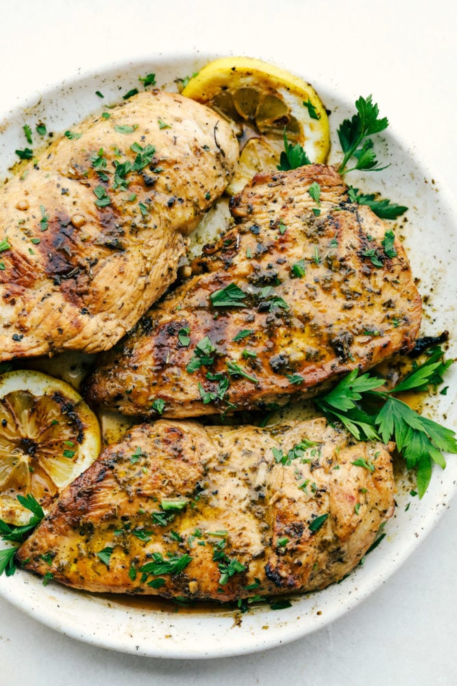This absolutely perfect chicken marinade will make your chicken so tender and juicy you will be amazed!!ย This will be the one recipe that you use on repeat all summer! Cooked marinated chicken on a plate with green garnish.