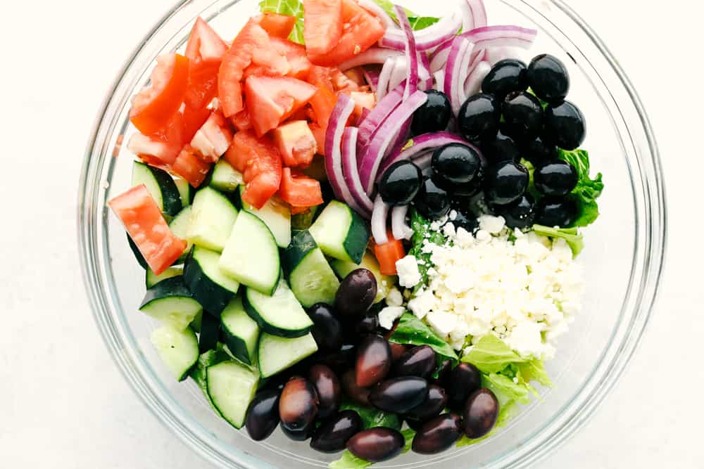 Greek Salad is a fresh, crunchy, vibrant salad with the BEST Greek dressing! Every bite is packed with color and the best flavors that will keep you digging in for more! Greek Salad ingredients in a clear bowl.