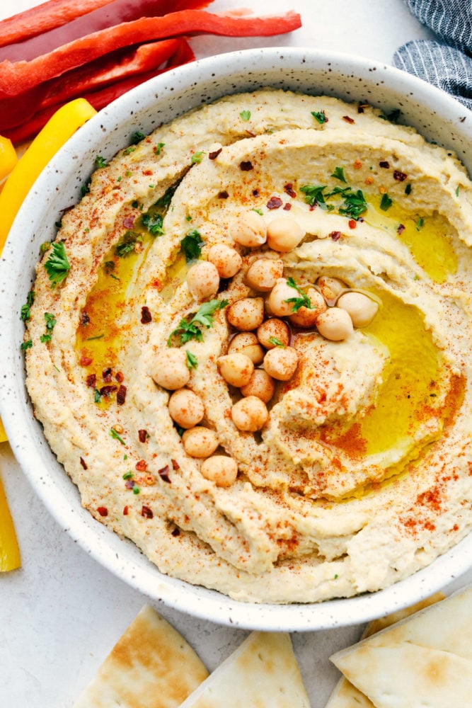 This is the BEST hummus that is fresh, flavorful, smooth and creamy plus quick and easy to make. Add this hummus for your next dip! Hummus in a white speckled bowl with chickpeas garnished over top.