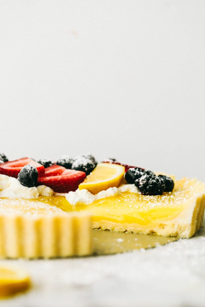 This sweet and savory lemon tart dessert is pure heaven and melts in your mouth with every bite! From the buttery shortbread crust, to the sweet and creamy lemon curd then topped with fresh fruit and powdered sugar, this dessert is rich and flavorful.ย Lemon tart photo of a side of the dessert with fresh berries on top and powdered sugar.