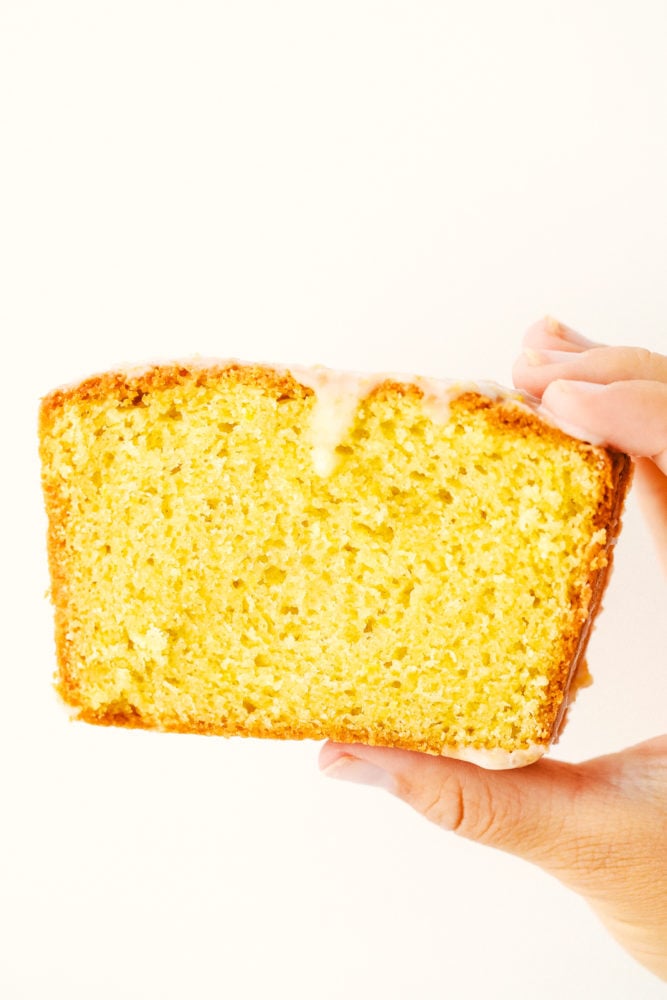 Glazed Lemon Bread is a soft, moist bread bursting with citrus lemon flavor and topped with a shell of sweet lemon glaze. This quick and easy homemade bread is great for sharing or savoring!! Slice of glazed lemon bread in a photo being held up by a hand.