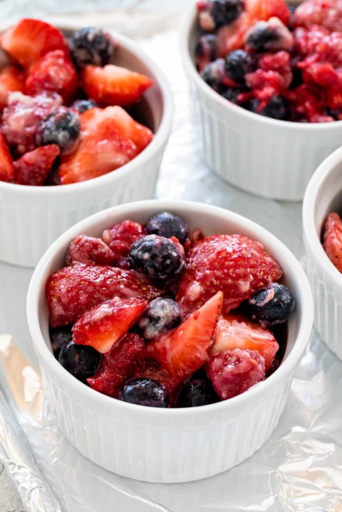 Mixed berry crisp is a colorful combination of fruit with a crunchy oat topping. These smaller individual portions baked in a ramekin make it easy to serve. The warm dessert tastes incredible topped with whipped cream or ice cream. fruit in white ramekins