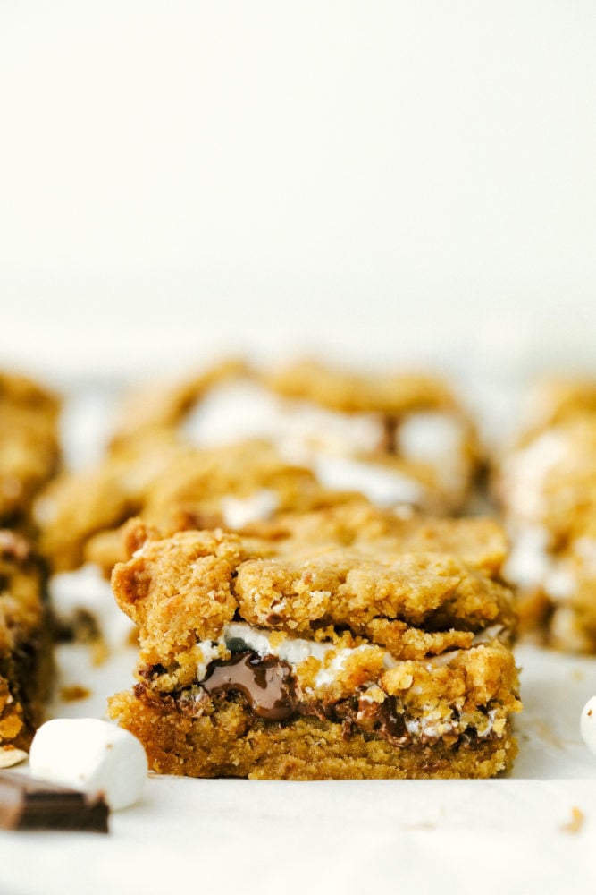 Ooey Gooey S'mores Bars are a delicious treat inspired by campfire s'mores with melty marshmallow, a buttery graham cracker crust, and a rich-sweet chocolate.ย These satisfying and easy to make bars are irresistible! Close up on a square of ooey gooey smores bars.