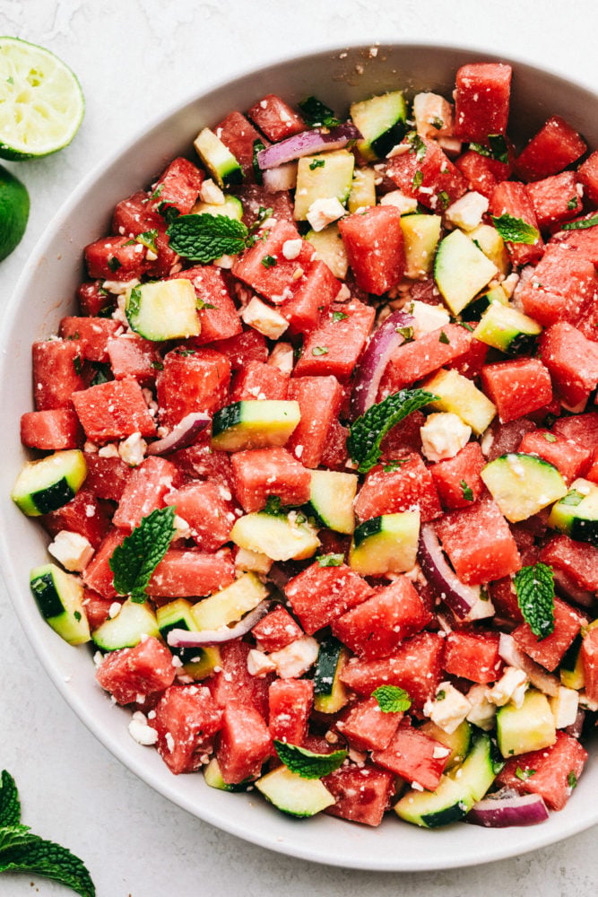 Watermelon Salad is bursting with flavors from the juicy watermelon and salty feta cheese, then topped off with hints of lime and mint.ย It is the perfect fresh sweet and savory mix of flavors that just scream summer!! Watermelon salad in a white bowl.