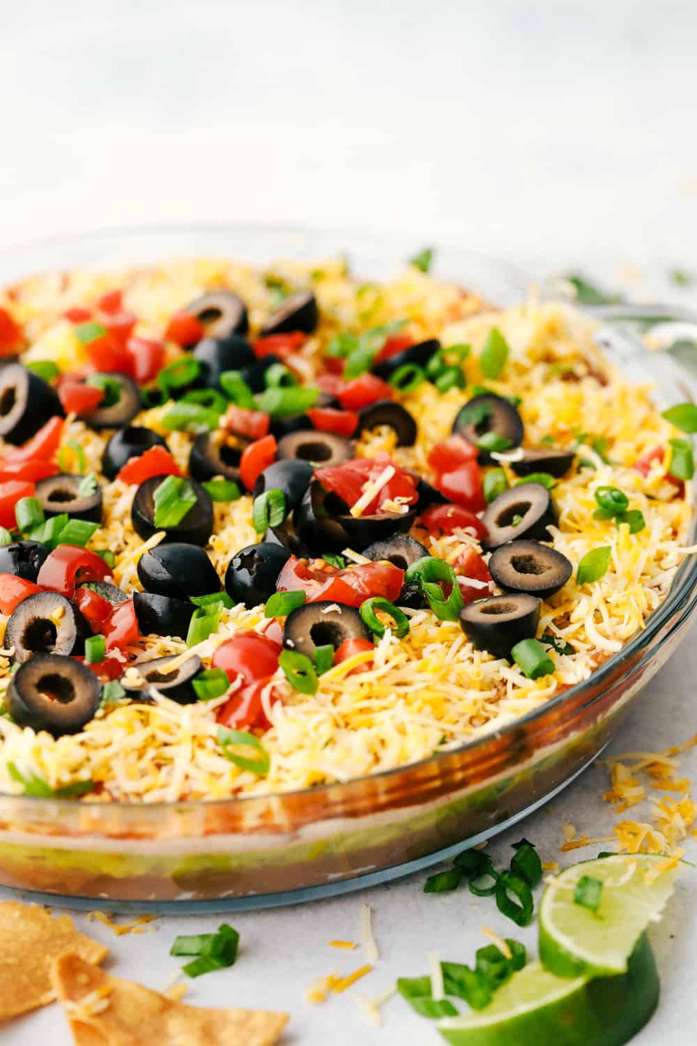 Awesome 7 Layer Dip is an addicting creamy dip that includes all your favorites, like guacamole, refried beans, and sour cream! You will be amazed at how simple it is to put together such an incredibly delicious dip! Angle shot of 7 layer dip in a serving dish.