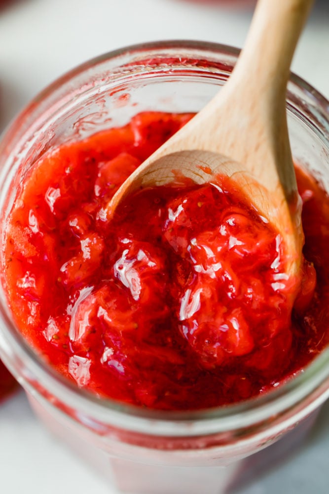 Homemade Strawberry Jam use all those fresh, juicy berries to make your own jam at home! No canning required. Simply store this jam in your refrigerator or freezer to enjoy. Strawberry jam in a jar with a wooden spoon in it.