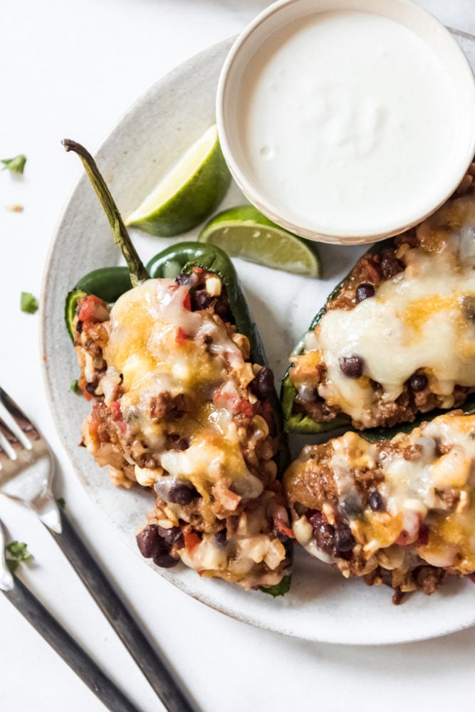 Stuffed Poblano Peppers are loaded with southwest seasoned ground beef, rice, veggies, and cheese for a satisfying dinner with just a little bit of a kick! Everybody raves about this twist on classic stuffed peppers! Stuffed poblano peppers on a plate next to a bowl of crema.
