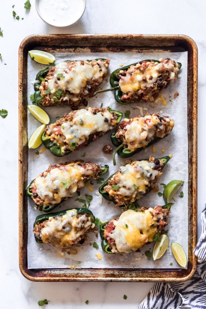 Stuffed Poblano Peppers are loaded with southwest seasoned ground beef, rice, veggies, and cheese for a satisfying dinner with just a little bit of a kick! Everybody raves about this twist on classic stuffed peppers! Eight stuffed poblano peppers topped with melted cheese on a baking sheet with lime wedges.