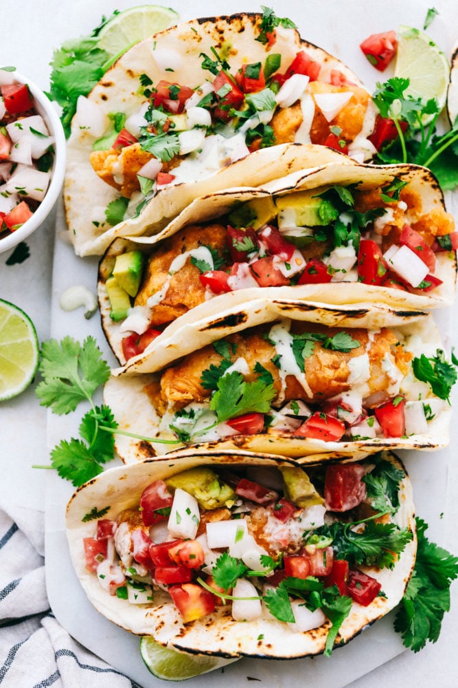 Baja Fish Tacos are made with with crispy beer battered cod and topped with pico de gallo and the perfect cilantro ranch dressing. Every bite of the fried fish is bursting with flavor but is still light and fresh enough for a perfect summer meal! Finished baja tacos on a plate.
