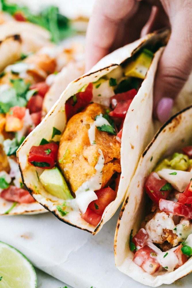 Baja Fish Tacos are made with with crispy beer battered cod and topped with pico de gallo and the perfect cilantro ranch dressing. Every bite of the fried fish is bursting with flavor but is still light and fresh enough for a perfect summer meal! Picking up a finished baja taco.