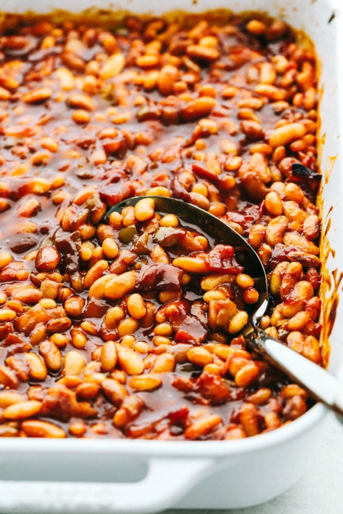 ย I am showing you how to make the best baked beans from start to finish. ย Making homemade baked beans is a lot easier than you think! Scooping up baked beans with a serving spoon.