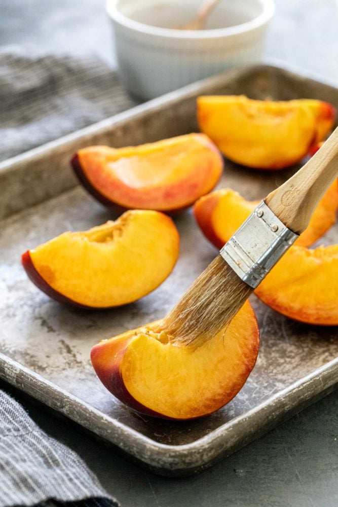 Brown sugar grilled peaches are a summertime delight. Ripe peaches are lightly charred on the barbecue then sprinkled with a sweet spiced topping that transforms into a glaze. Perfect as a quick dessert or add it to a fresh salad.ย quartered peaches on a sheet tray