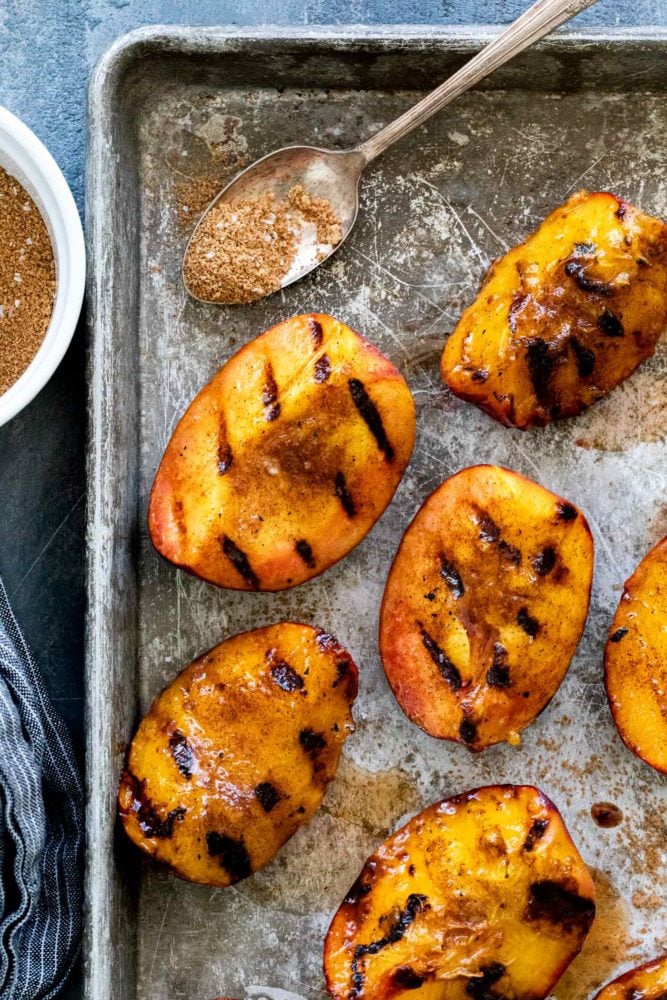 Brown sugar grilled peaches are a summertime delight. Ripe peaches are lightly charred on the barbecue then sprinkled with a sweet spiced topping that transforms into a glaze. Perfect as a quick dessert or add it to a fresh salad.ย grilled peaches on a sheet tray