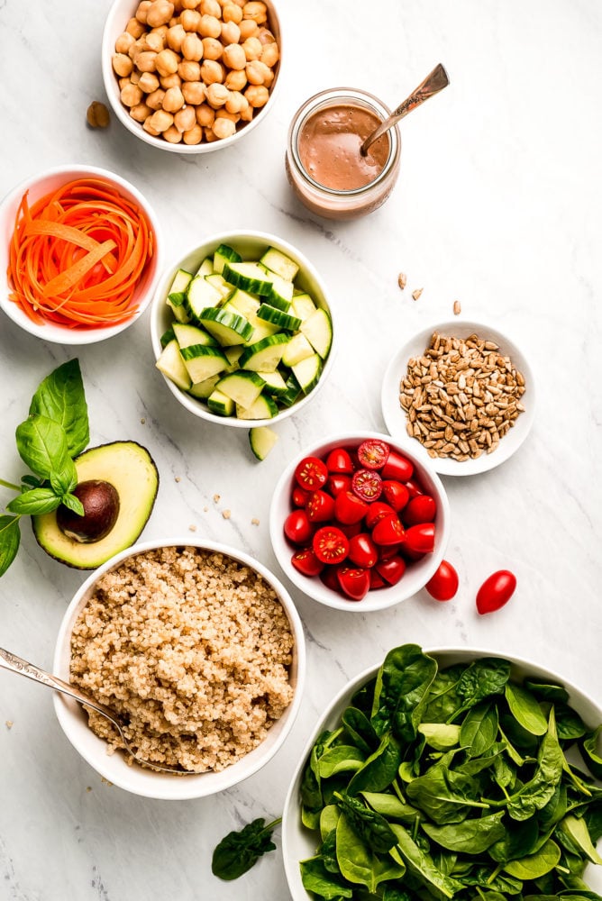 This Vegan Buddha Bowl is loaded with colorful raw summer vegetables, whole grains, good fats, and topped with a tangy creamy balsamic dressing. Make adjustments to use up whatever vegetables you have on hand and enjoy this delicious vegan meal for lunch or dinner all summer long! Various size bowls of vegetables, quinoa, seeds, chickpeas, and dressing.