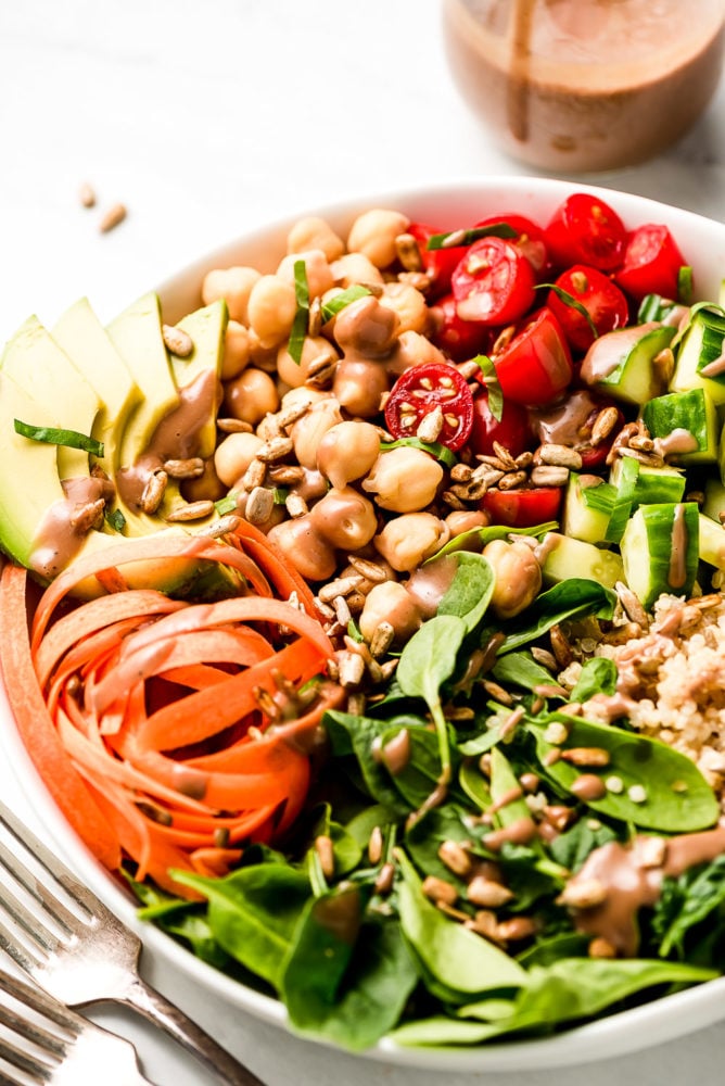 This Vegan Buddha Bowl is loaded with colorful raw summer vegetables, whole grains, good fats, and topped with a tangy creamy balsamic dressing. Make adjustments to use up whatever vegetables you have on hand and enjoy this delicious vegan meal for lunch or dinner all summer long! A close up shot of chickpeas and vegetables in a bowl.