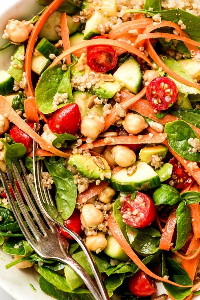 This Vegan Buddha Bowl is loaded with colorful raw summer vegetables, whole grains, good fats, and topped with a tangy creamy balsamic dressing. Make adjustments to use up whatever vegetables you have on hand and enjoy this delicious vegan meal for lunch or dinner all summer long! A salad of spinach, cucumbers, grape tomatoes, carrot ribbons, avocado, chickpeas, and quinoa all mixed together.