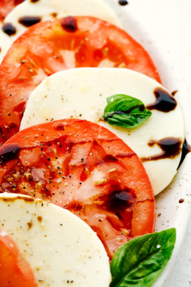 Caprese Salad is made with layers of fresh tomato slices, basil, and mozzarella cheese, then drizzled with balsamic glaze and topped with a sprinkle of salt and pepper. It is the perfect summer meal that you will crave all year! Close up on caprese salad.