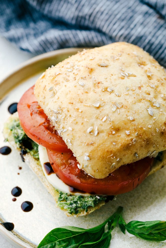 A Caprese Sandwich with Basil Pesto is a thick ciabatta bread stuffed with layers of tomato, mozzarella, and fresh pesto.ย Add a drizzle of a balsamic glaze and you will have a homemade sandwich that is better than anything you could buy at a restaurant! A finished caprese sandwich on a plate.