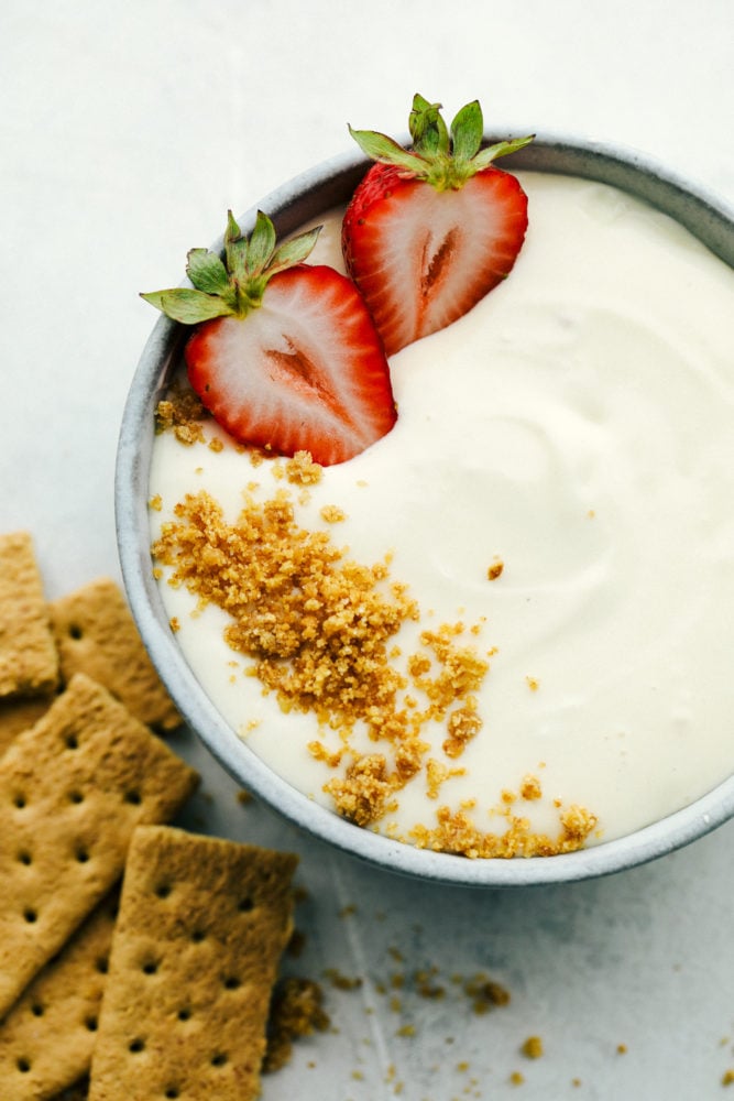 2 Ingredient Cheesecake Dip is a super easy to make, sweet and tangy dip. It is so creamy and perfect for dipping fruit as a cool summer snack or dessert! Graham cracker crumbles and strawberries garnishing cheesecake dip.