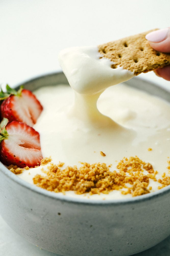 2 Ingredient Cheesecake Dip is a super easy to make, sweet and tangy dip. It is so creamy and perfect for dipping fruit as a cool summer snack or dessert! Dipping a graham cracker into cheesecake dip.