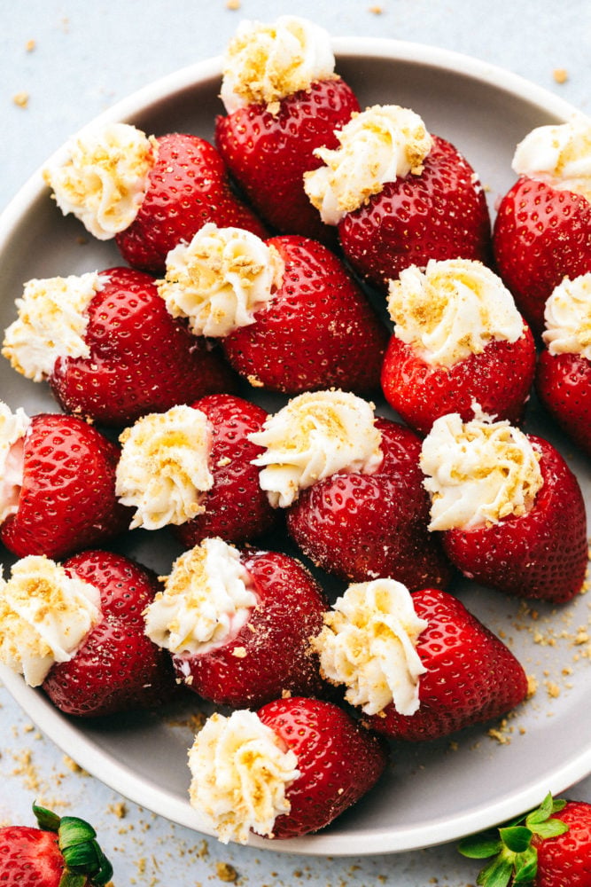 Cheesecake stuffed strawberries are the perfect party treat filled with a creamy and smooth cream cheese filling. Topped with a graham cracker crumb, they are juicy, tangy, and sweet all at the same time. This easy and quick dessert is unbelievably delicious and impossible to resist! A plate filled with cheesecake stuffed strawberries.