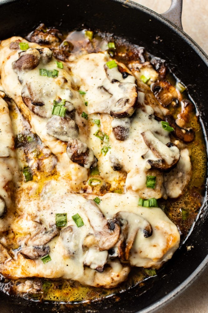 Chicken Lombardy is an insanely delicious cheesy version of Chicken Marsala baked to perfection with mozzarella and scallions. Ready in about 30 minutes! Chicken Lombardy close-up in a cast iron skillet