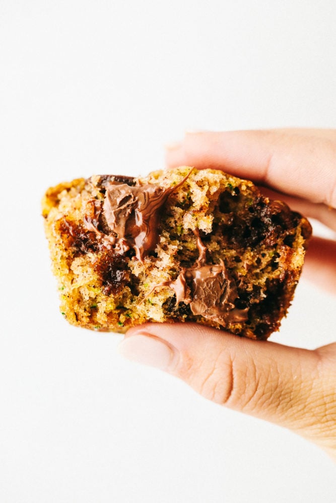 Chocolate Chip Zucchini Muffins are moist and rich muffins that are loaded with flavor from rich chocolate and shredded zucchini!ย They will be a huge hit and will give you a great way to use all that zucchini from your garden! One chocolate chip zucchini muffin being held in the air with a white background.