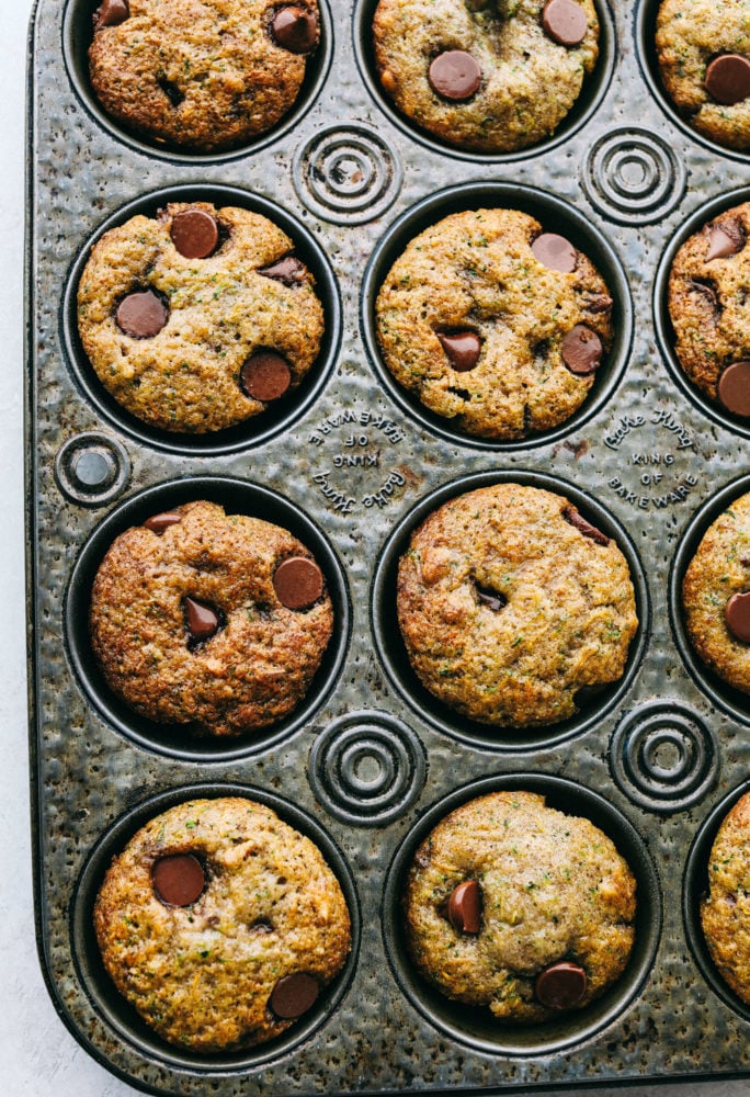 Chocolate Chip Zucchini Muffins are moist and rich muffins that are loaded with flavor from rich chocolate and shredded zucchini!ย They will be a huge hit and will give you a great way to use all that zucchini from your garden! Chocolate chip zucchini muffins in a baking pan.