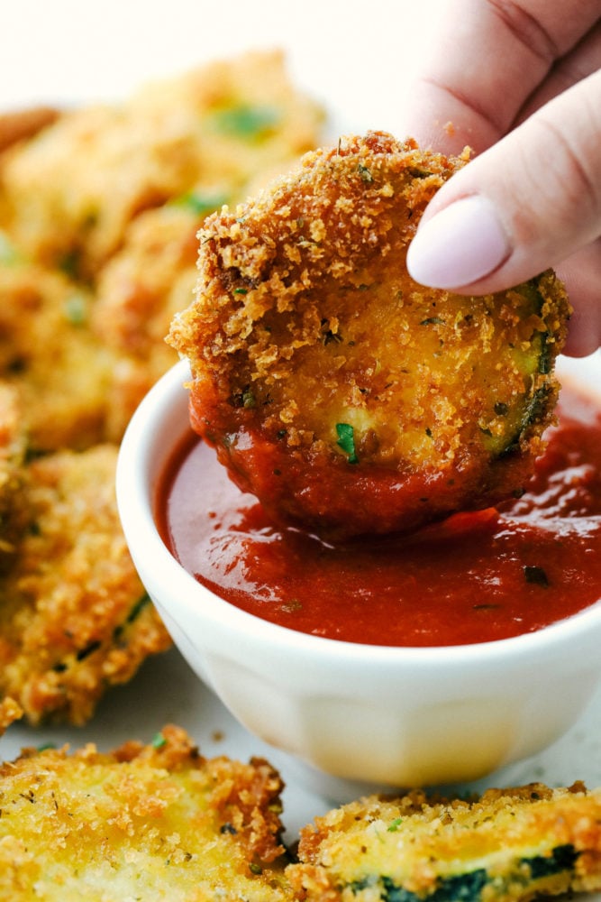 Crispy Parmesan Fried Zucchini is made with savory parmesan and panko coated zucchini bites. They will quickly become a favorite for an easy and crowd-pleasing snack, appetizer or side dish! Dipping a zucchini slice in marinara sauce.