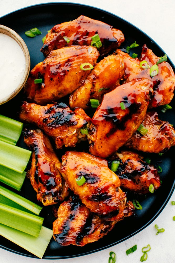 Grilled Honey Buffalo Chicken Wings are perfectly tender and juicy on the inside with a crispy skin on the outside that is drenched in a sweet and spicy honey buffalo sauce.ย The flavors are so irresistible you will not be able to stop eating them! Grilled Honey Buffalo Wings on a black plate with celery and white dip.