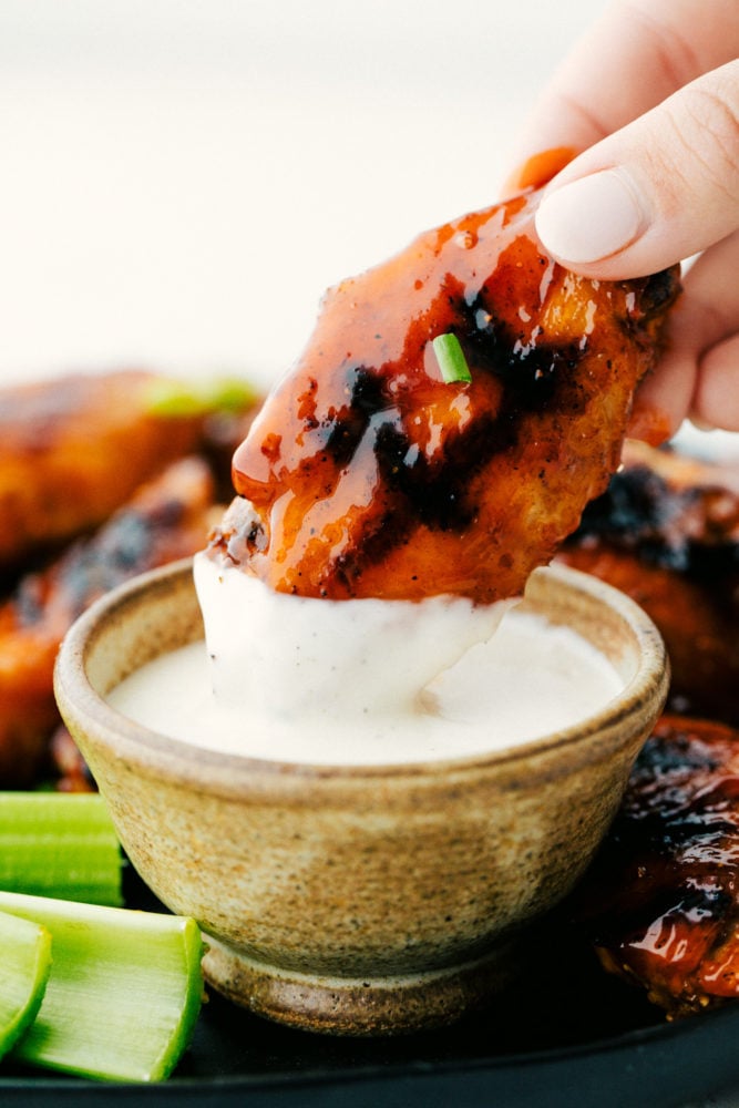 Grilled Honey Buffalo Chicken Wings are perfectly tender and juicy on the inside with a crispy skin on the outside that is drenched in a sweet and spicy honey buffalo sauce.ย The flavors are so irresistible you will not be able to stop eating them! Dipping a chicken wing into white sauce.