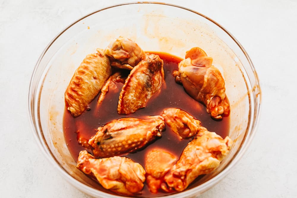 Grilled Honey Buffalo Chicken Wings are perfectly tender and juicy on the inside with a crispy skin on the outside that is drenched in a sweet and spicy honey buffalo sauce.ย The flavors are so irresistible you will not be able to stop eating them! Marinating chicken wings in a clear bowl.