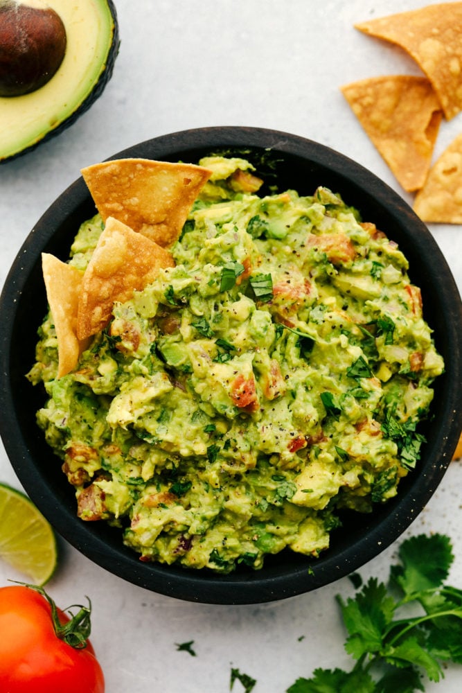 Guacamole is the perfect creamy dip that's loaded with avocado and tomatoes and spiced with jalapeno and cumin. Beware because this crowd-pleasing dip is such a hit it disappears quickly! Guacamole in a black bowl.