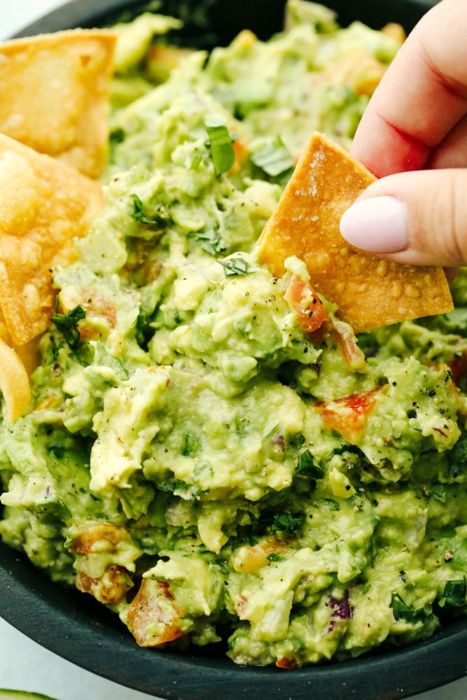 Guacamole is the perfect creamy dip that's loaded with avocado and tomatoes and spiced with jalapeno and cumin. Beware because this crowd-pleasing dip is such a hit it disappears quickly! Dipping a chip into guacamole.