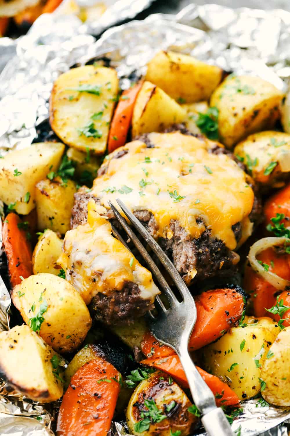 These delicious filled hobo dinners are perfect for cooking a mixture of carrots, potatoes and your meat all in a foil packet. It is fun to make and an easy dinner option for the summertime!ย Hobo dinner with foil hamburger being cut with a fork over top of vegetables.