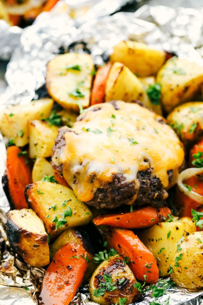 These delicious filled hobo dinners are perfect for cooking a mixture of carrots, potatoes and your meat all in a foil packet. It is fun to make and an easy dinner option for the summertime!ย Up close photo of the foil packets opened with vegetables and a hamburger patty.