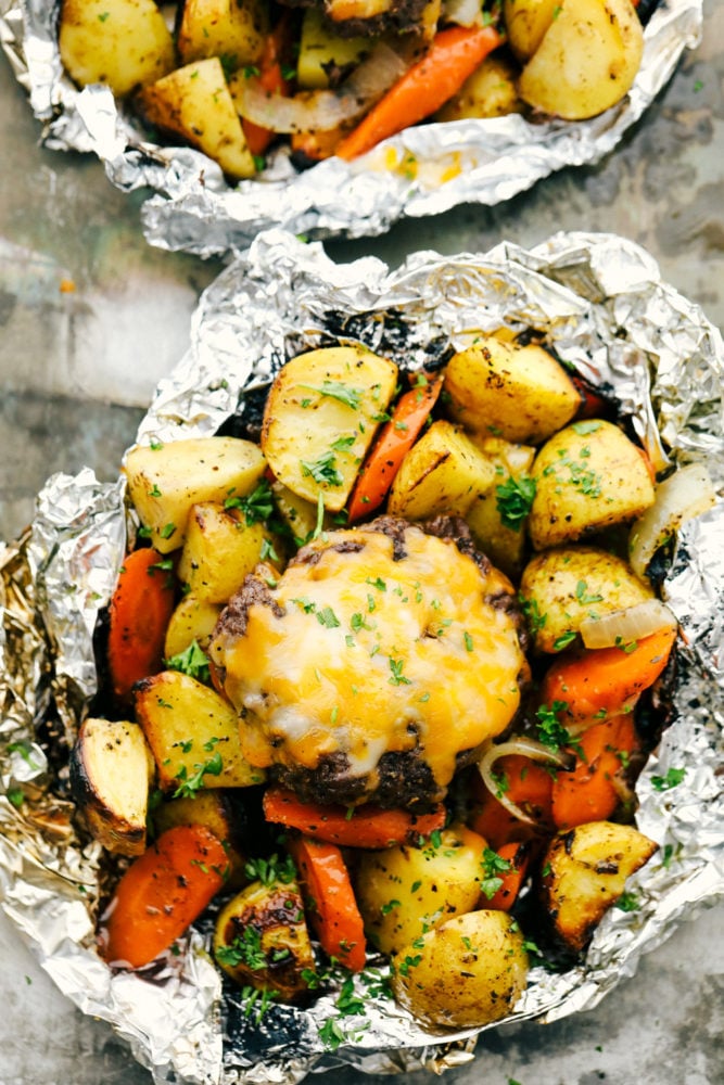 These delicious filled hobo dinners are perfect for cooking a mixture of carrots, potatoes and your meat all in a foil packet. It is fun to make and an easy dinner option for the summertime!ย Hobo dinner foil packets opened with vegetables and hamburger patty on top with a slice of cheese.