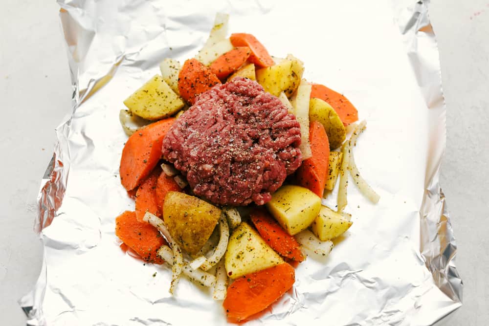You know those nights when everyoneโs hungry and youโre one eye twitch away from serving cereal? My easy Hobo Dinner Foil Packets, packed with hearty veggies and juicy beef, are the answer! Foil with a pile of seasoned veggies topped with a seasoned ground beef patty.