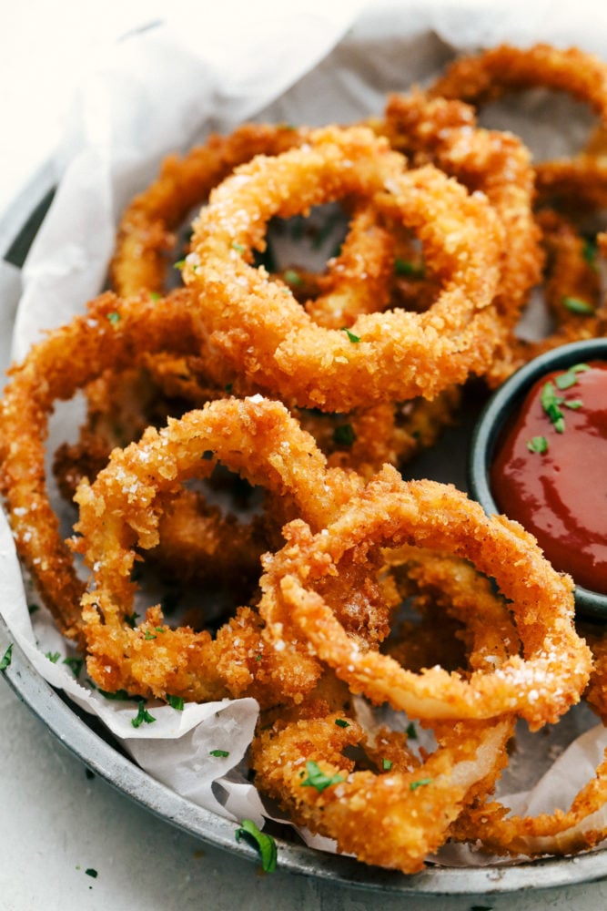 Crispy Onion Rings whether baked or fried will be a huge hit appetizer that you will want to make again and again. The sweet onion wrapped in a crunch of perfectly crispy panko breading is just as delicious as any restaurant version, and surprisingly easy to make at home! Finished onion rings on a plate with dipping sauce.