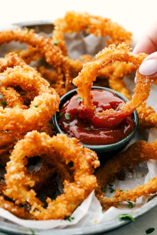 Crispy Onion Rings whether baked or fried will be a huge hit appetizer that you will want to make again and again. The sweet onion wrapped in a crunch of perfectly crispy panko breading is just as delicious as any restaurant version, and surprisingly easy to make at home! Dipping onion rings in sauce.